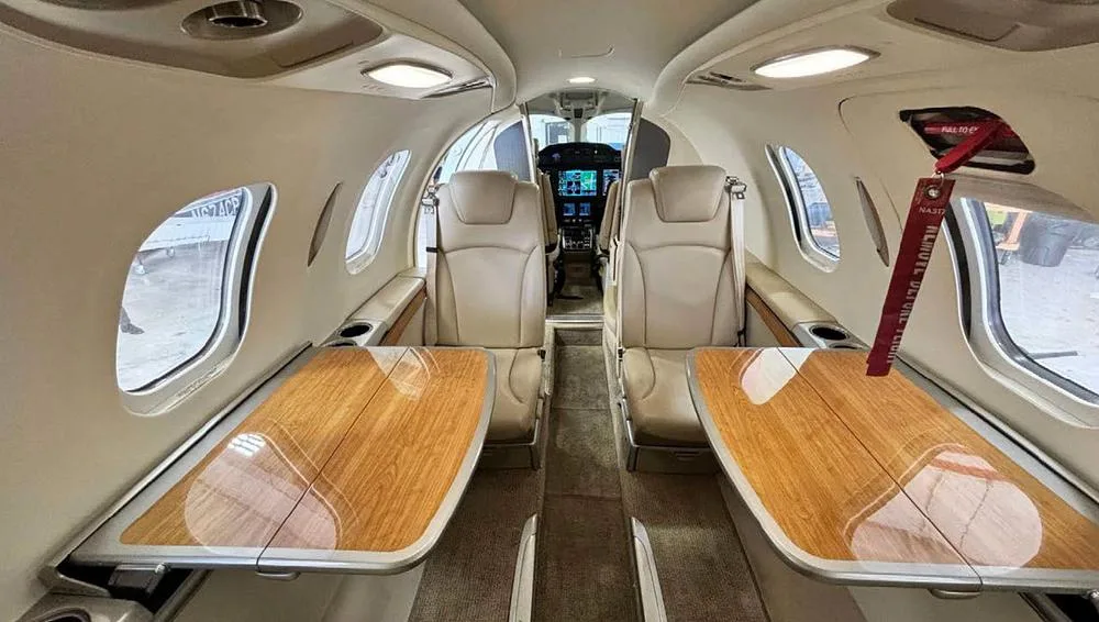 The aircraft's interior cabin with beige seats and wooden tables, looking towards the cockpit.