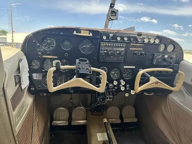 The cockpit of a small aircraft, featuring a dark instrument panel with various gauges and two light-colored control yokes.