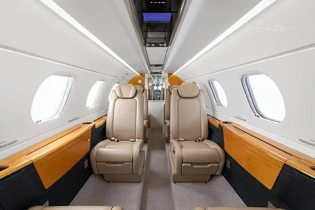 The interior cabin of a business jet featuring light brown leather seats and elegant wood trim.