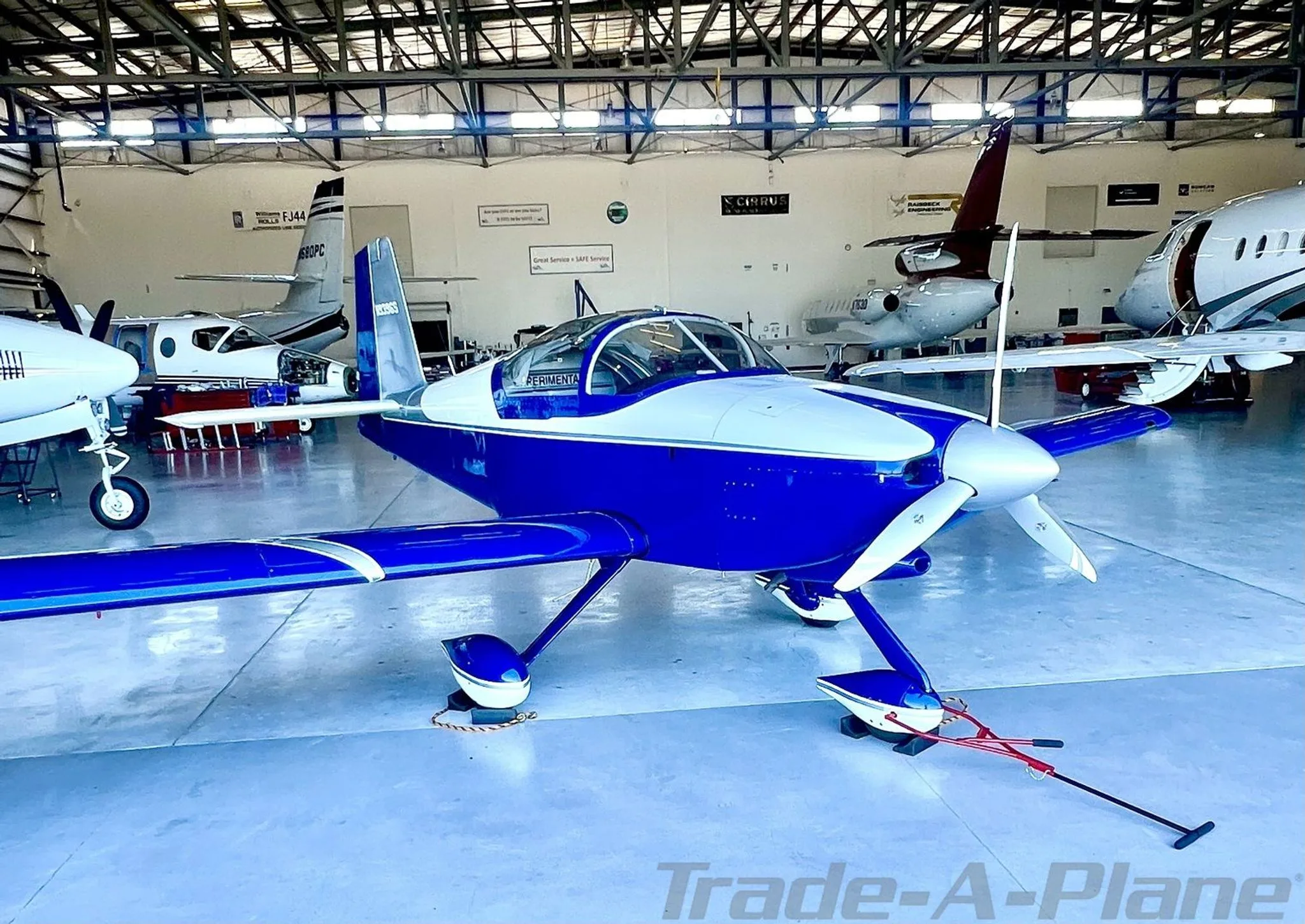 The aircraft is parked inside a hangar with other planes in the background.