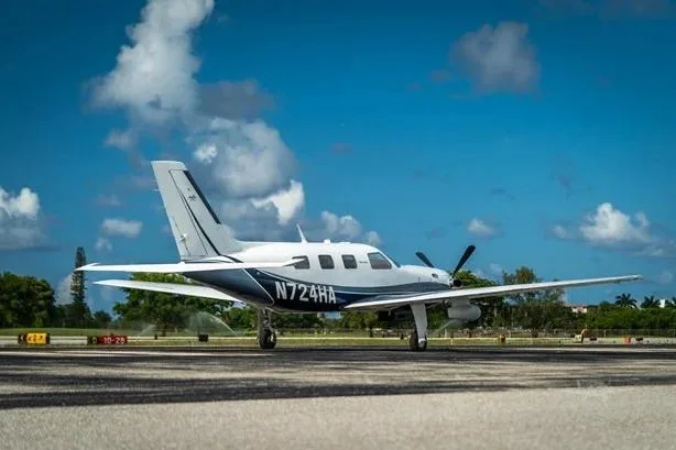 A white and blue Piper M500 (Meridian) aircraft, registration N724HA, parked on a tarmac with a clear blue sky.