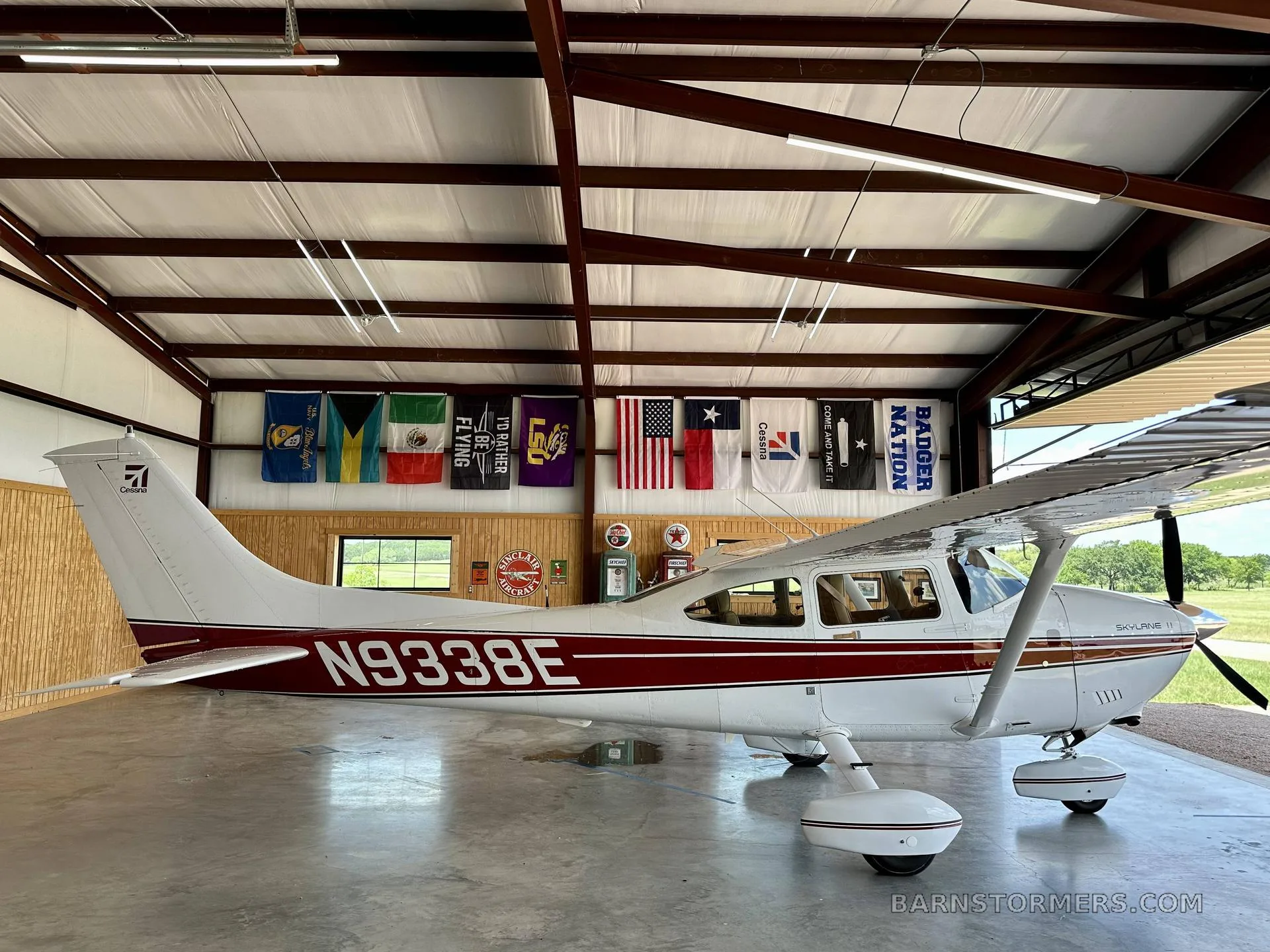 A white Cessna Skylane II with red stripes and registration N9338E is parked inside a hangar, viewed from the side.