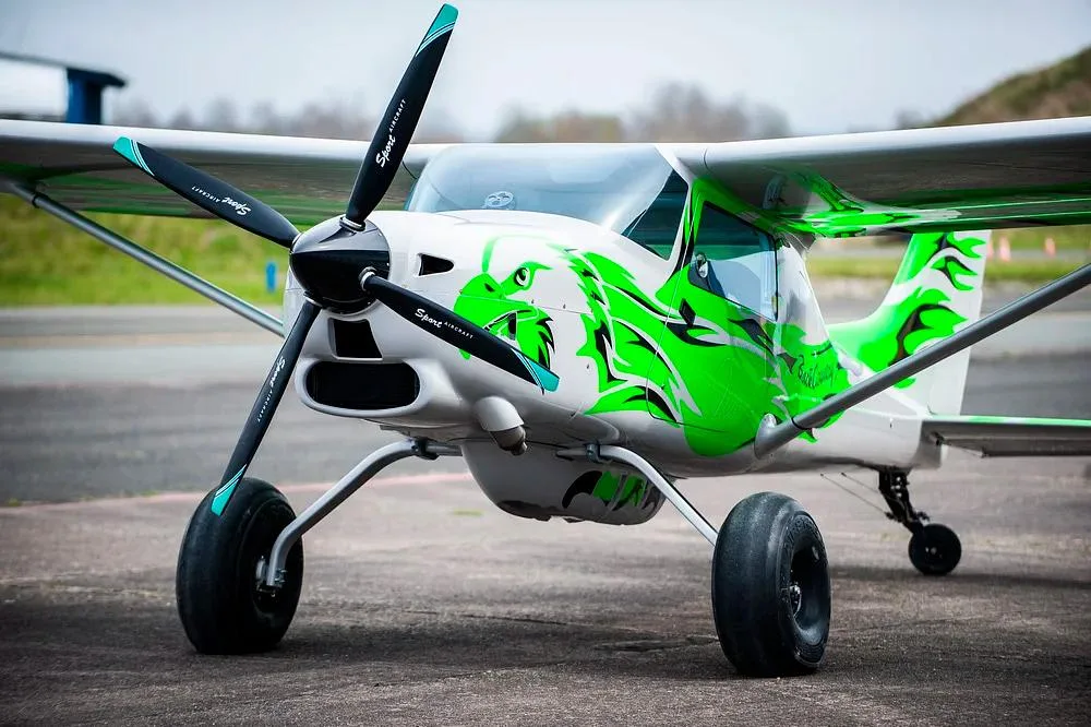 A close-up front view of the white and green Backcountry Super Cub aircraft with a dragon paint scheme.