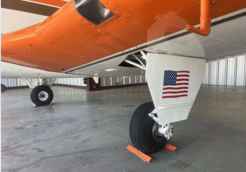 A close-up view of the main landing gear and orange wing underside of a Beechcraft Bonanza, featuring an American flag decal.