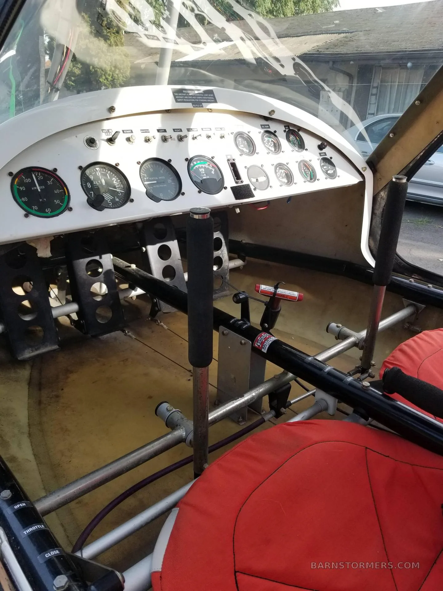 The open cockpit of an ultralight aircraft, showing the instrument panel, controls, and red seats.