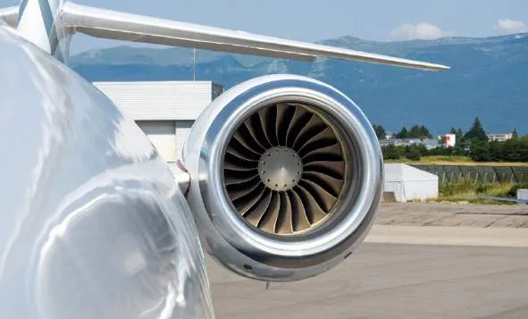 A close-up view of the jet engine on the tail of a white business jet, with mountains in the background.