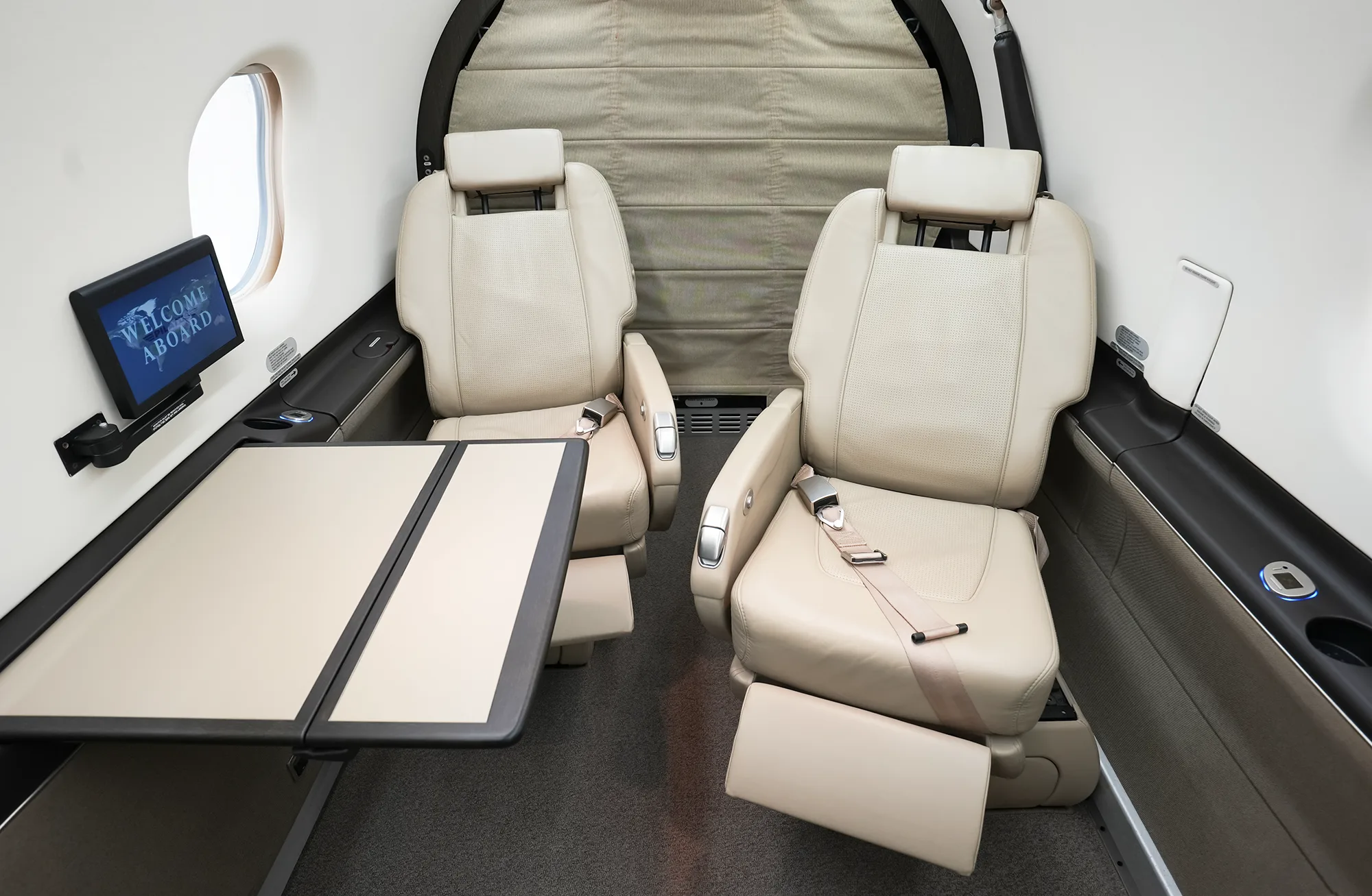 A close-up view of two beige leather cabin seats with a fold-out table extended between them.
