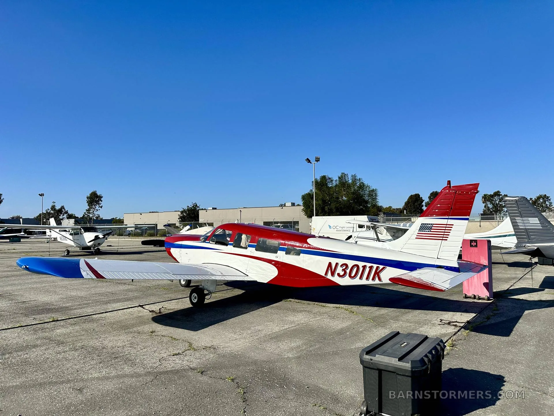 A side view of a red, white, and blue single-engine propeller aircraft (N3011K) with an American flag on its tail.