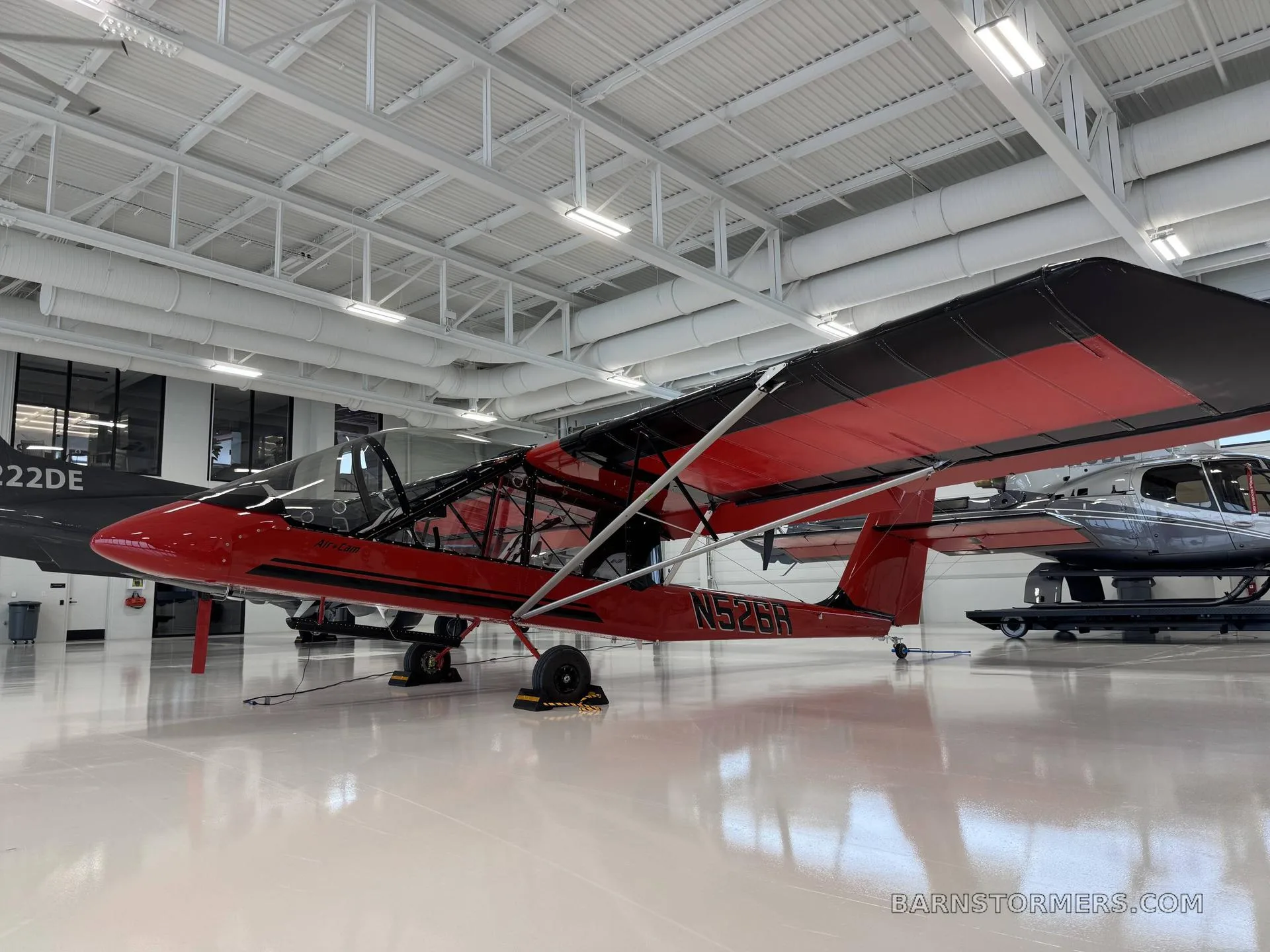 A red and black Air-Cam aircraft with registration N526R is parked in a clean, modern hangar.