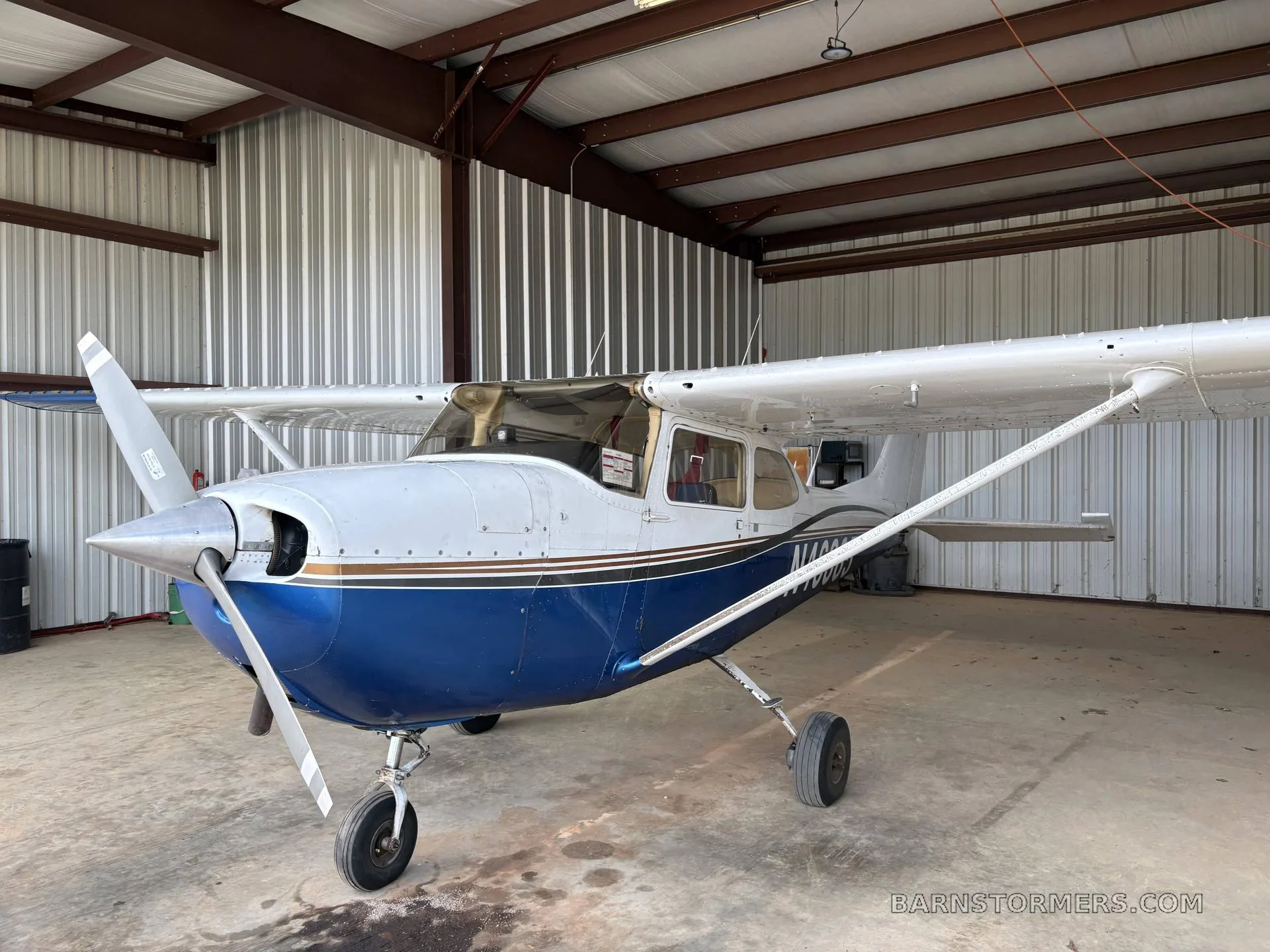 A blue and white single-engine propeller aircraft with a dark stripe, parked inside a metal hangar.