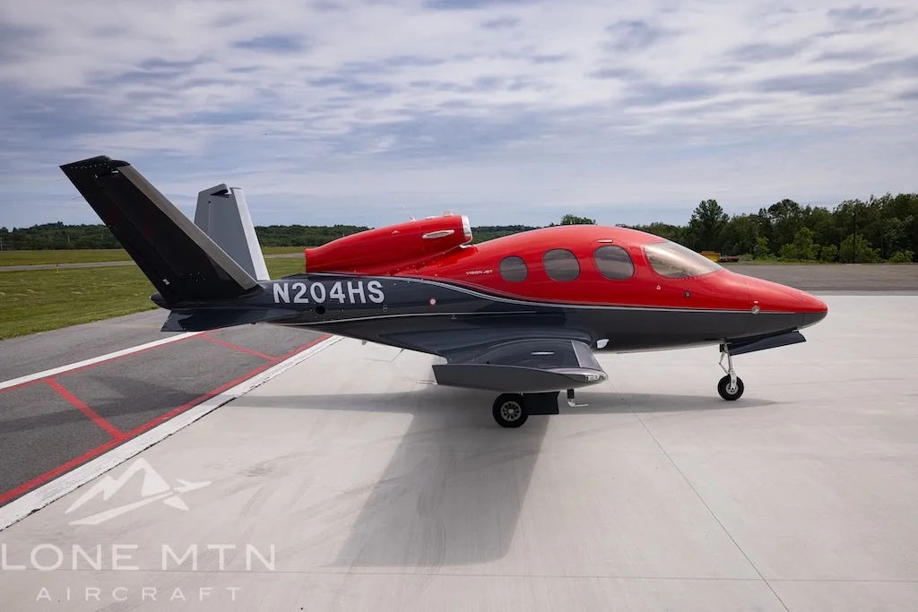 A side view of the Cirrus Vision Jet N204HS in red and grey, parked on an airfield.