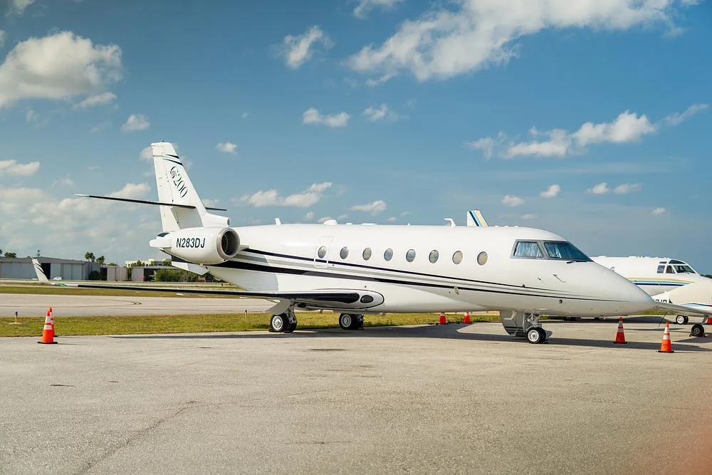 A white Gulfstream G200 business jet, tail number N283DJ, is parked on an airport tarmac with orange cones around it.