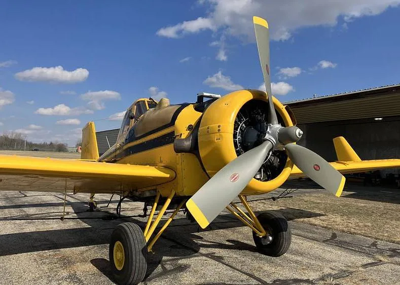 A three-quarter front view of a yellow agricultural aircraft, showing its propeller, landing gear, and fuselage.