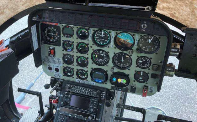The cockpit instrument panel of a helicopter, featuring numerous analog gauges and a digital display unit.