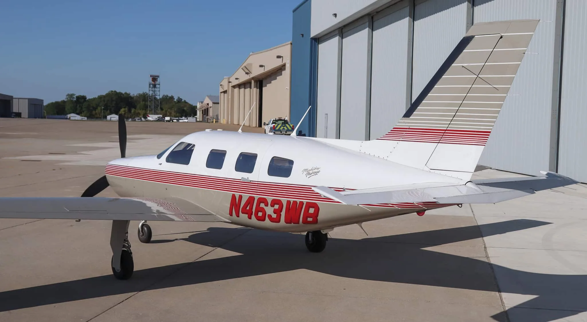 A rear-quarter view of the Piper Malibu Mirage N463WB parked on an airport tarmac in front of hangars.