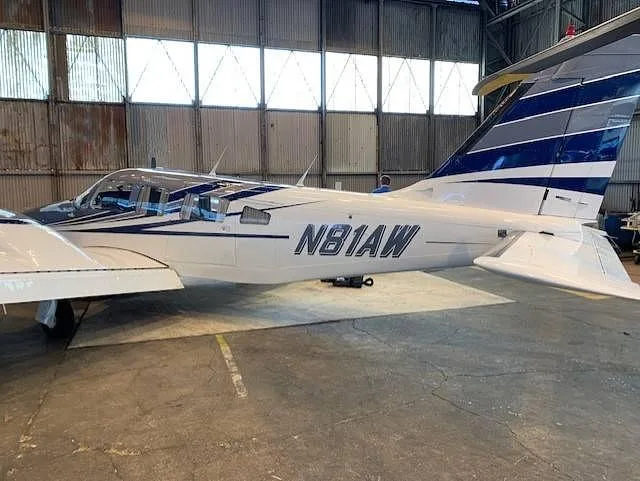 Side view of the white and grey twin-engine aircraft (N81AW) with blue stripes inside a hangar.