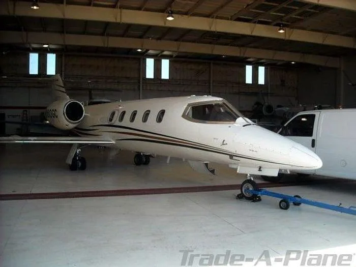 A white Learjet 35A with gold and brown stripes, registration N160GC, being towed inside a hangar.