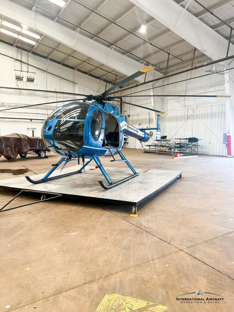 A wide shot of the blue N69VS helicopter with white stripes, parked on a platform in a large hangar.