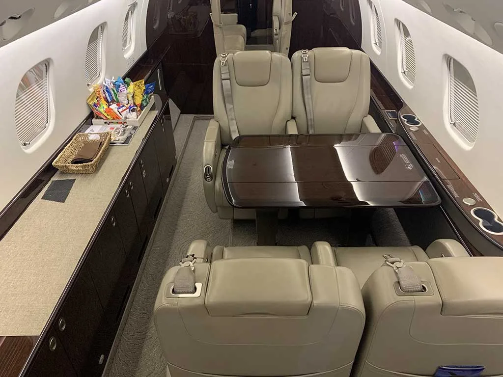 A view inside the Embraer Legacy 650 cabin, showing beige seats, a deployed table, and a snack basket.