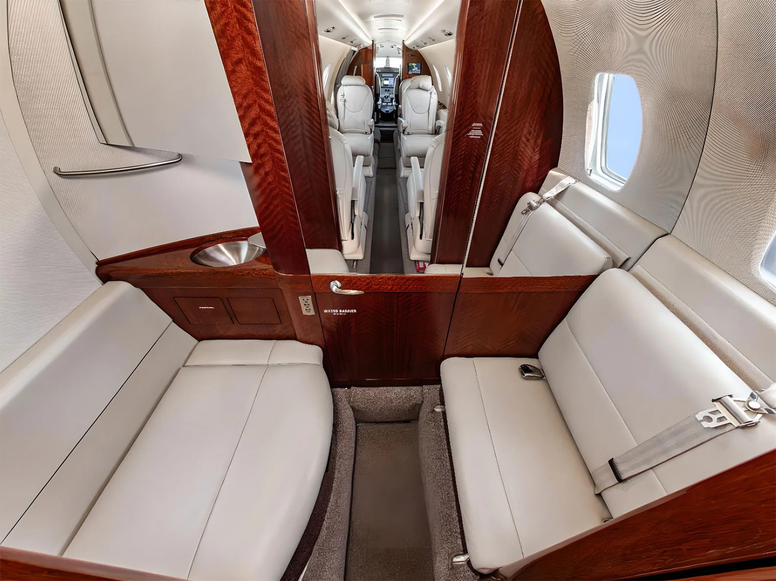 The rear section of a private jet cabin with two opposing light leather divan seats and dark wood cabinetry.