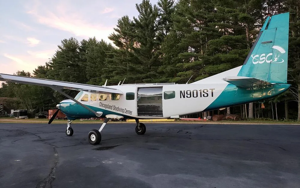 A teal and white single-engine turboprop aircraft, N901ST, is parked on an airfield surrounded by pine trees.