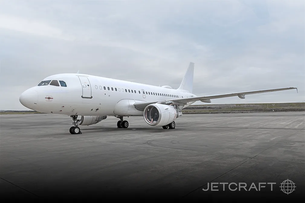 A white Airbus A319 or A320 aircraft parked on an airfield under a cloudy sky.