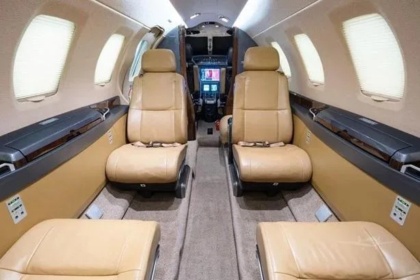 The tan leather interior of a private jet cabin looking forward towards the cockpit.