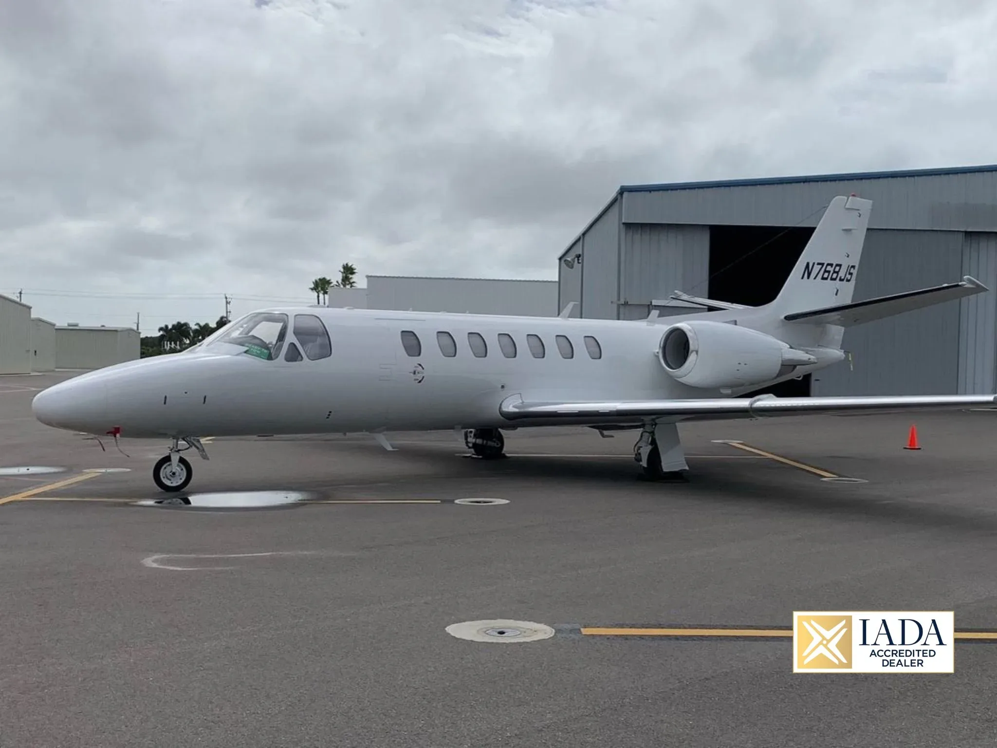 A white Cessna Citation business jet is parked on a tarmac next to a hangar under a cloudy sky.