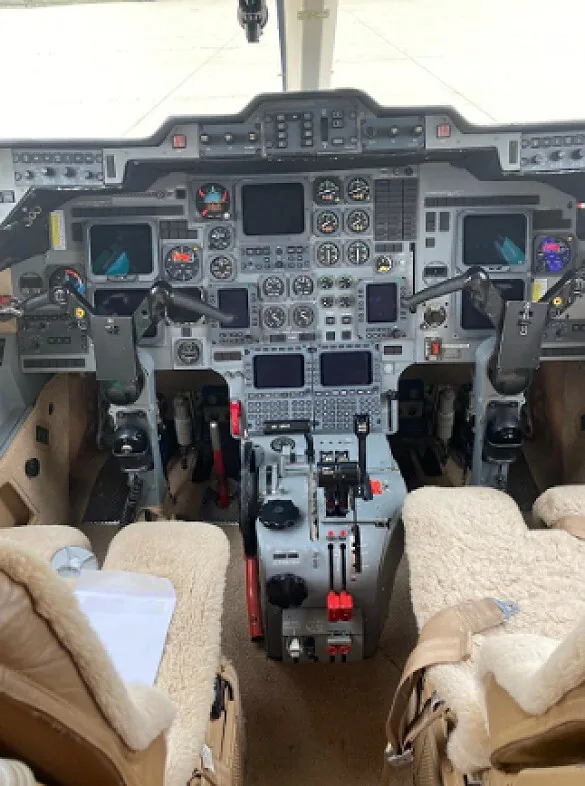 The cockpit of an aircraft, showing the instrument panel, controls, and two sheepskin-covered seats.