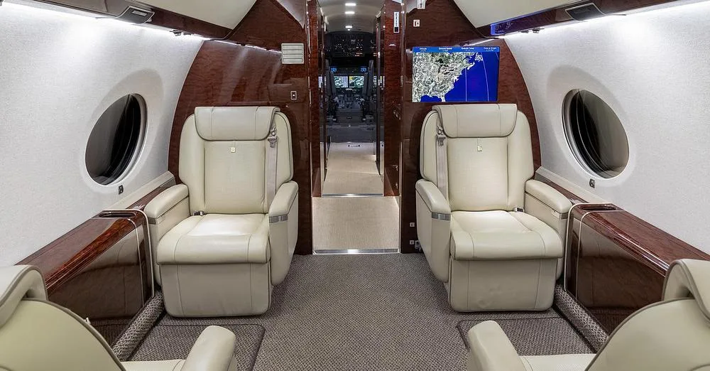 The Gulfstream G650 cabin interior with two facing light leather seats and a large map display screen.