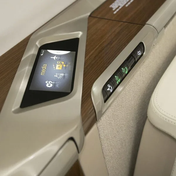 A close-up of a private jet's cabin control panel with a digital screen displaying media options and physical buttons for lighting.