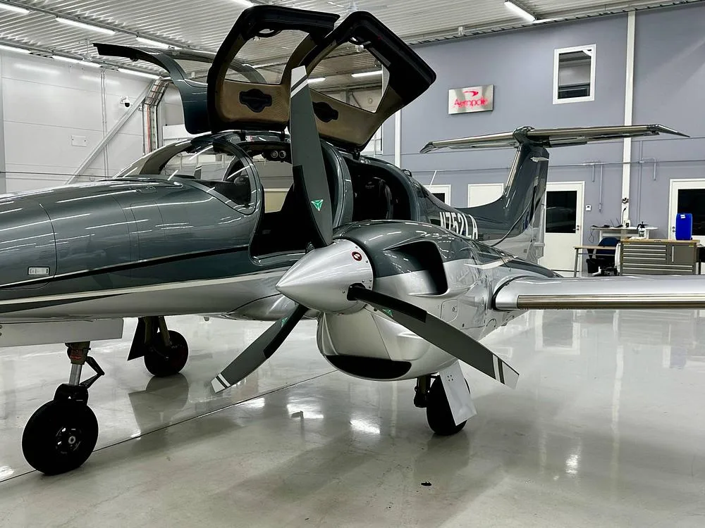 A front-right view of a gray and silver Diamond DA62 aircraft with registration N752LA, parked in a hangar with its doors open.