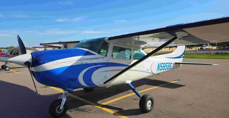 A white and blue Cessna 182 aircraft, registration N58586, parked on an asphalt tarmac.