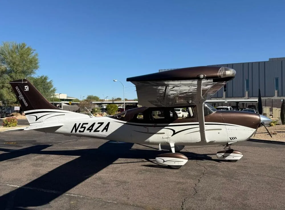 A three-quarter rear view of a brown and white Cessna 206 Stationair aircraft (N54ZA) on a tarmac.