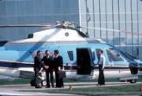 A group of people standing in front of a blue and white helicopter.