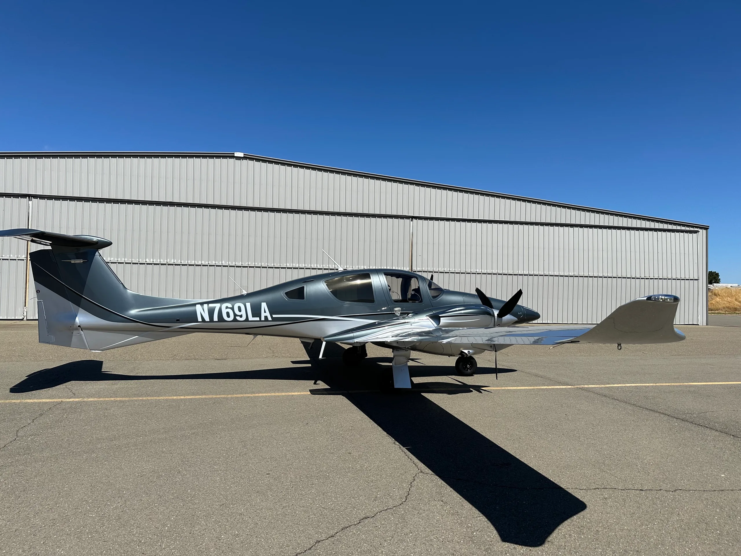 A side view of a grey and silver Diamond DA62 aircraft with registration N769LA parked on an airfield.