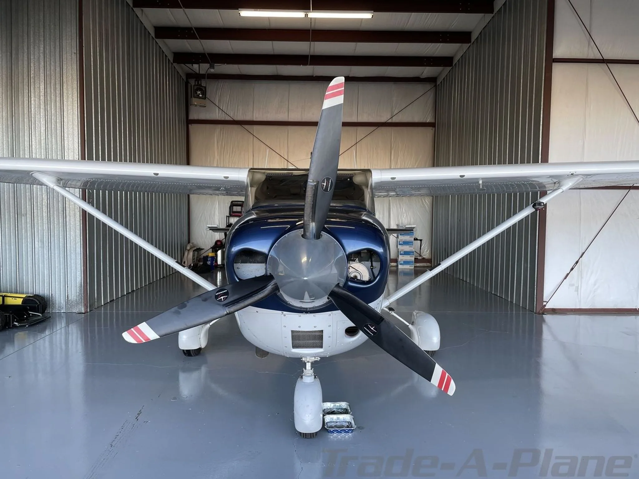 A front view of a blue and white Cessna 182 aircraft with a three-bladed propeller, parked in a hangar.