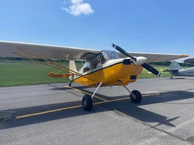 A yellow and white high-wing aircraft with a propeller is parked on an asphalt runway under a clear blue sky.