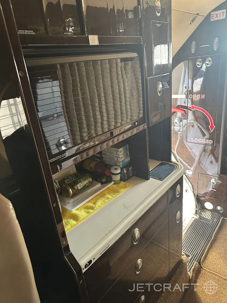 A dark wood galley area in a private jet cabin with a counter and storage compartments.