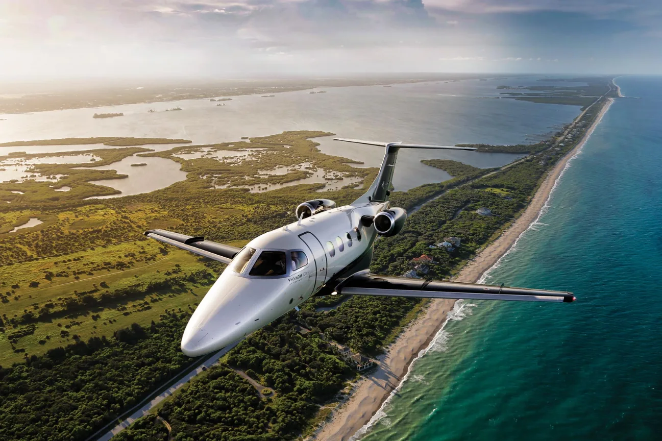 A white and silver jet aircraft flying over a coastline.