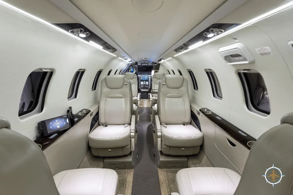 A wide view of a luxurious aircraft cabin with multiple rows of light-colored leather seats and screens on the side panels.