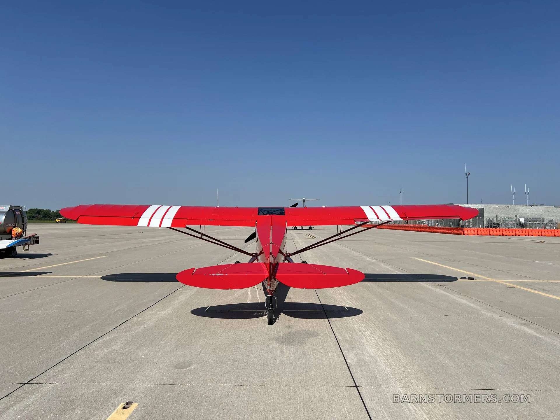 A rear view of a red PA-18 Supercub on the airport tarmac.