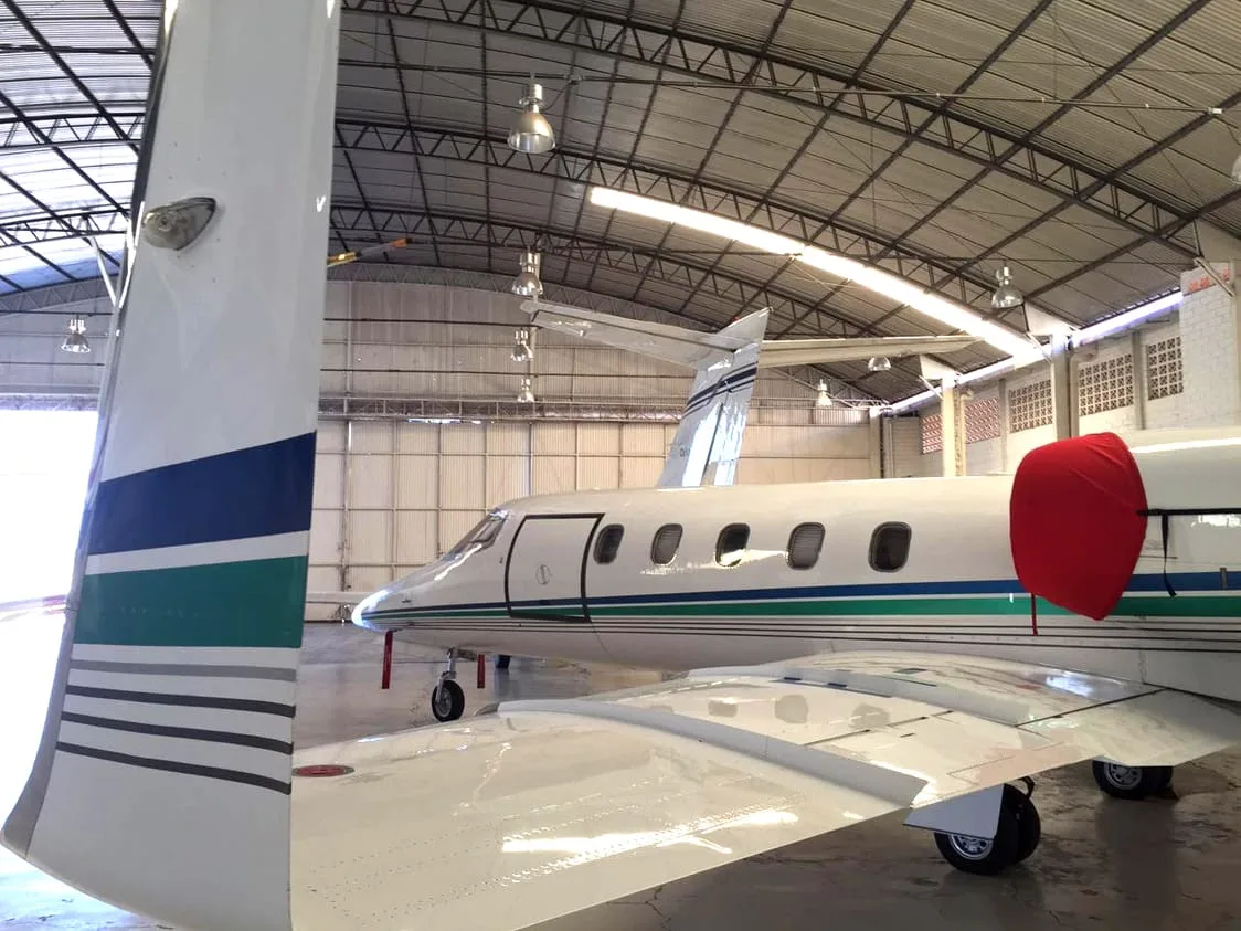 The tail and wing of a white Learjet with green and blue stripes, parked inside a hangar.