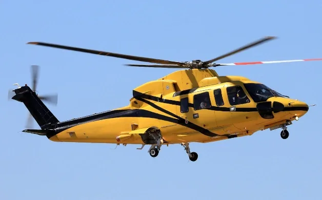 A yellow helicopter with black stripes is captured in flight against a clear blue sky.