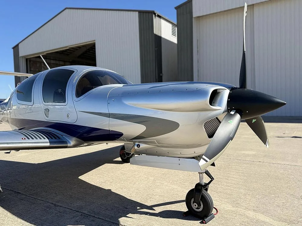 A close-up view of the nose and propeller of the silver and blue Diamond DA40 aircraft, N66RG, on the tarmac.