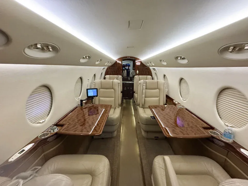 The luxurious interior cabin of a private jet with beige leather seats and polished wood tables.