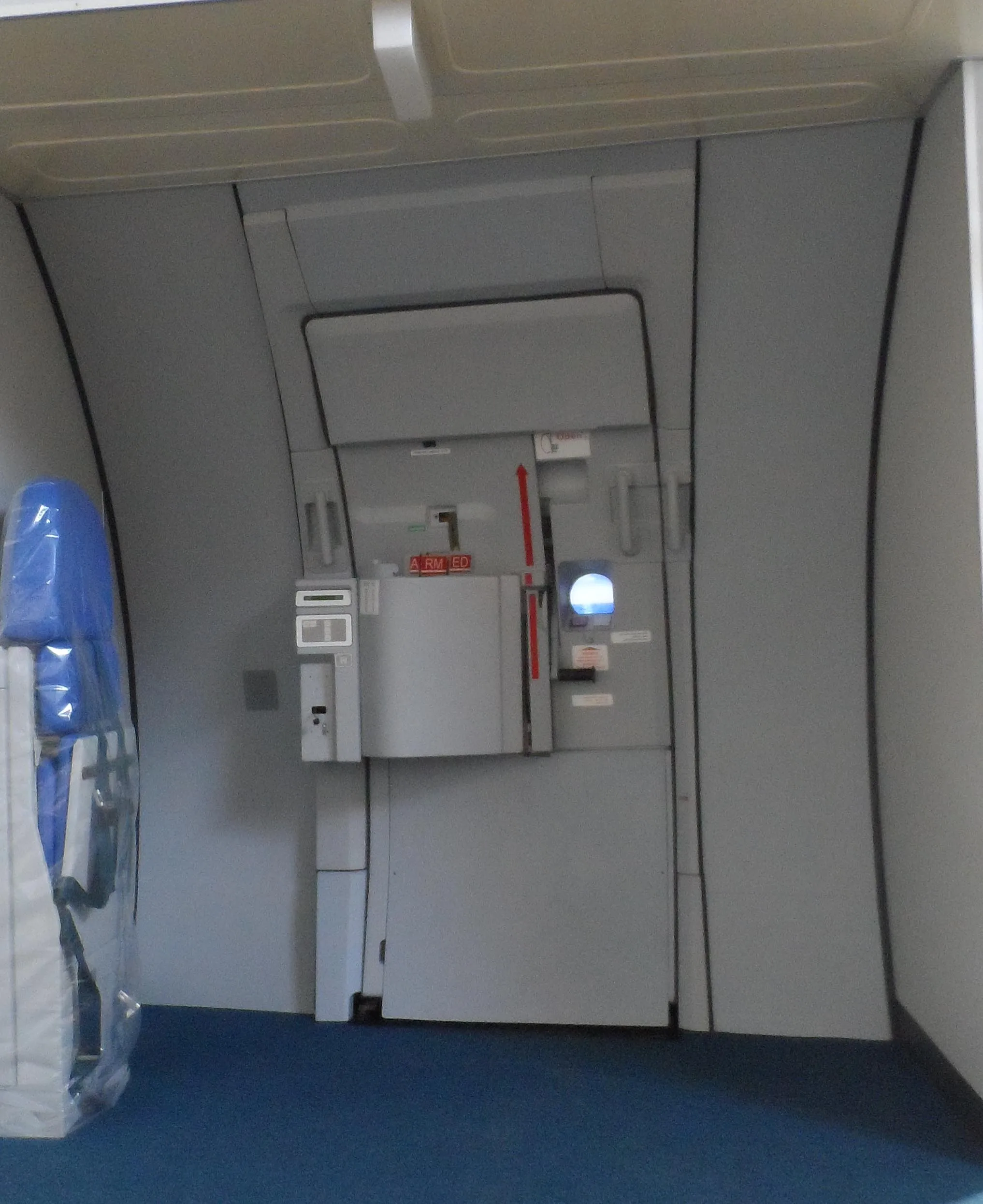 An aircraft cabin door with a wrapped blue seat to the left, showing the "ARMED" indicator.