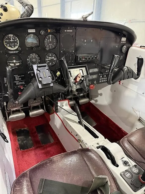 The cockpit of a Piper Tomahawk aircraft, showing the instrument panel, yokes, and red carpeted floor.