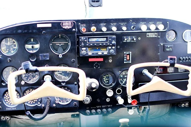 The cockpit instrument panel of an aircraft, featuring gauges, radios, and two control yokes.