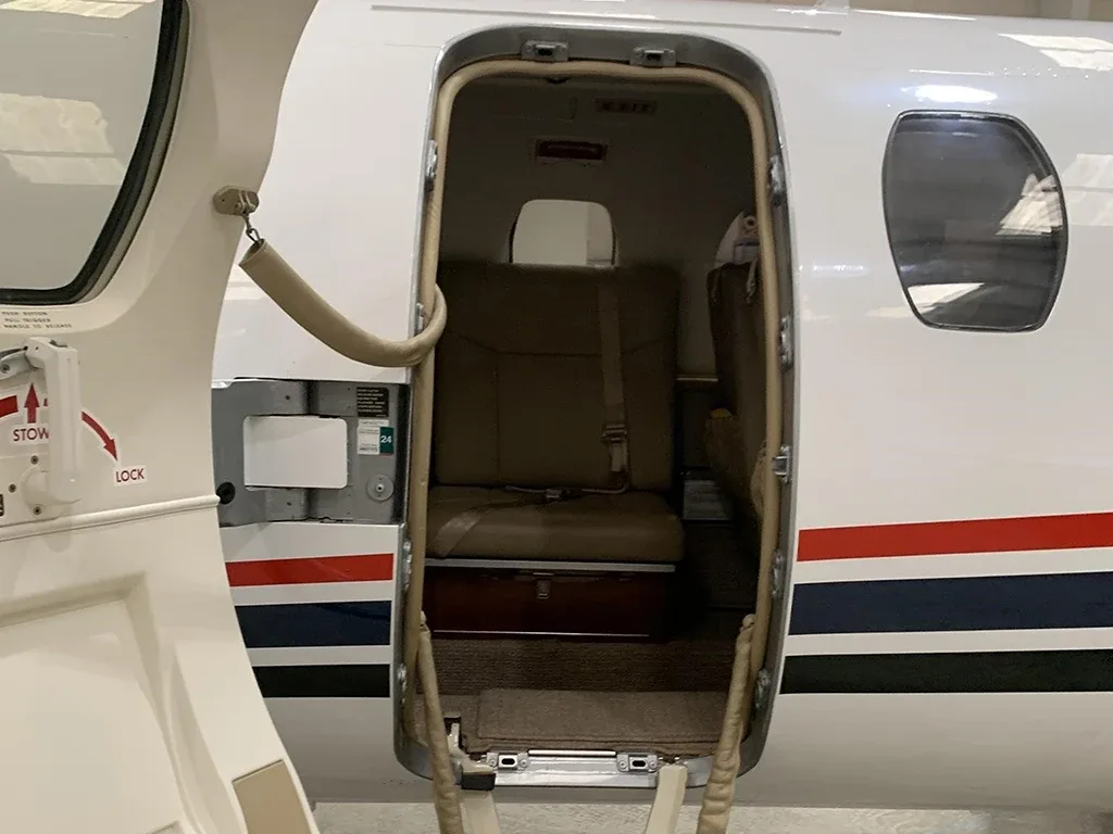 A close-up view looking into the aircraft cabin through the open main door, showing a beige seat and interior.